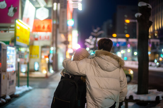 Asian couple dating and shopping at retail store street market together in the city at night. Man and woman enjoy and fun outdoor lifestyle nightlife walking city street in winter holiday vacation.