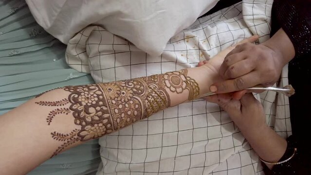 A Mehndi artist drawing a stunning Arabic design with Henna paste on a girl's hand during a Wedding ceremony in India.
