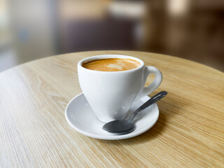 Coffee cup with saucer and spoon on a round wooden table