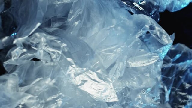 Vertical video. Plastic pollution. Ocean conservation. Waste disposal. Wet empty cellophane bags crushed bottles dump pile contamination on dark blue wrinkled texture background.