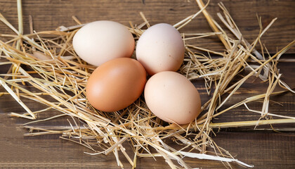 Three eggs in straw on wooden background.