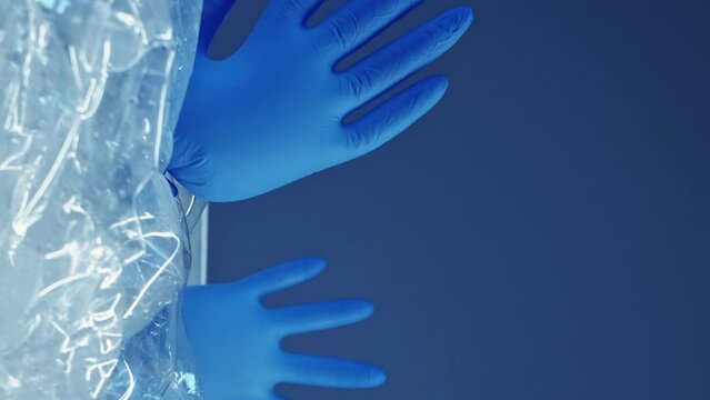 Vertical video. Ocean contamination. Waste reduction. Blown medical gloves in used creased wet bottles garbage pile isolated on glowing blue background empty space.