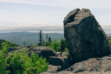 Fototapeta premium vue sur le sommet d'une montagne avec un gros rocher en avant plan une forêt dans la vallée lors d'une journée d'été