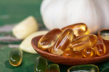 Close up of gold garlic extract capsules oil in wooden spoon.