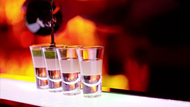 Barman making cocktail shots with liquor alcohol in three layers at the bar at night with red neon lights, slow motion