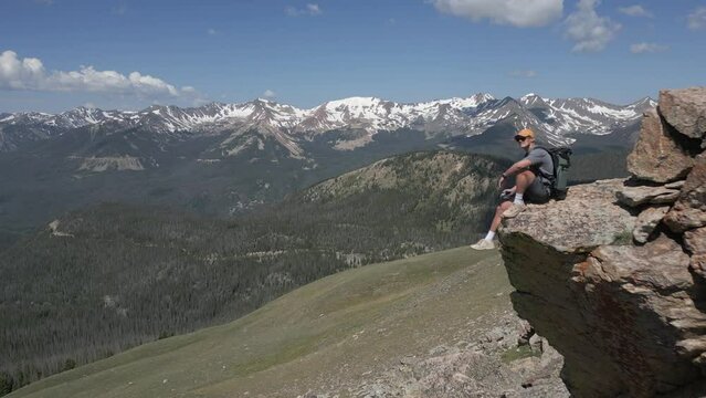 Man enjoys mountain peak view from rock on barren grass plateau
