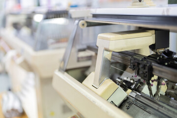 An image of a large weaving machine working with a computer. There are mechanisms and electrical working circuits. There is a spool of thread on top. in a large sewing industry
