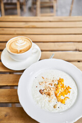 Breakfast in cafe on a sunny morning, on the summer veranda. Cappuccino coffee and rice porridge with mango, Cashews, sesame seeds. enjoying breakfast.