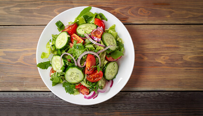 Salad with greens, cherry tomatoes, red onions and cucumber on white plate with wood background, overhead view