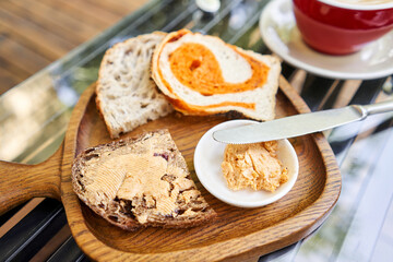 A slice of bread with butter on a chopping board. Assorted sliced bread on a wooden board. Served with smoked butter. Breakfast with cappuccino coffee. 