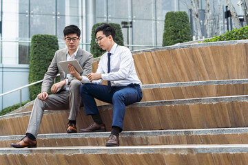 Asian business people using tablet computer and talking outdoors.