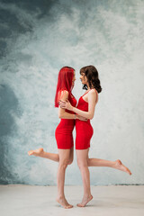 Full-length portrait of two tenderly embracing women dressed in identical red dresses. Lesbian intimacy.