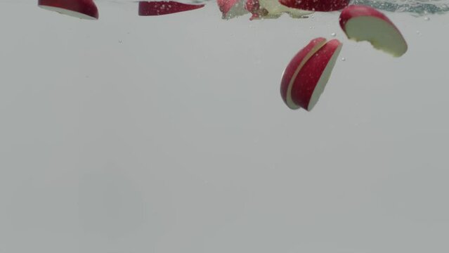 slow motion Red Delicious Apple slices falling into water.
