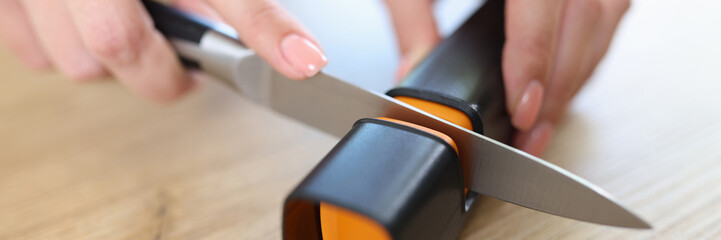 Woman sharpens knife with sharpener in kitchen close-up.
