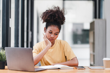 Young African American woman is taking notes in a notebook while watching a webinar video course. Afro american student listening to the lecture to study online through e-learning.