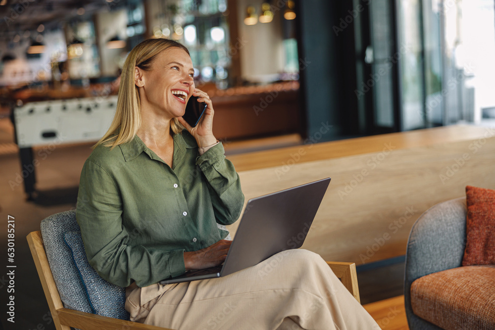 Wall mural Businesswoman is talking phone while sitting in coworking and work on laptop. Distance work concept