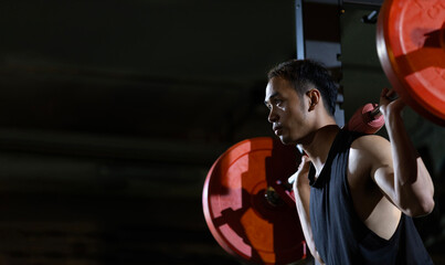 Asian muscular sport man is practice weight training on deadlift barbell for core muscle inside gym with dark background for exercising and workout concept