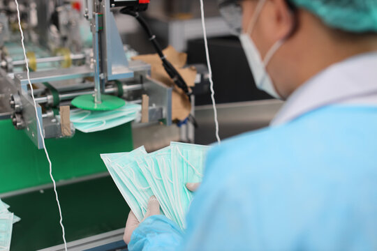 Rear view asian worker hands inspecting quality of mask and medical face mask production line, Industry and factory concept.