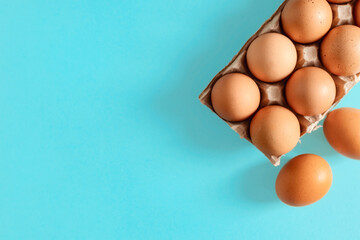 Brown eggs in a cardboard tray on a blue background with copy space