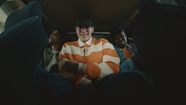 Low angle of Caucasian guy with two African American mates sitting in backseat of car and clubbing to hip hop music