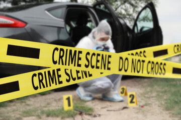 Yellow tapes blocking way to crime scene. Criminologist working outdoors