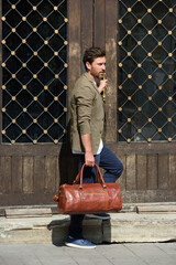 a man with a bag. black leather travel bag, street photo. man is wearing blue sneakers, jeans, a...