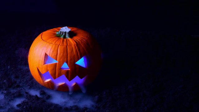 A pumpkin with its face cut out releases heavy smoke onto black ground. Halloween background.