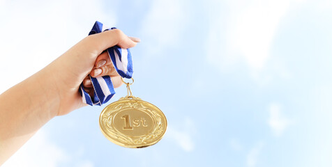 woman hand raised, holding gold medal against sky. award and victory concept