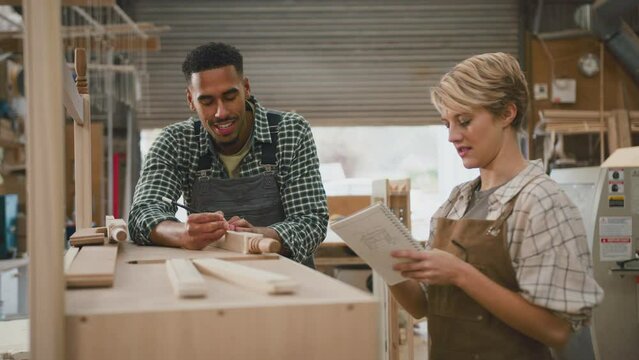 Male and female apprentice carpenters working in furniture workshop making notes and measuring wood - shot in slow motion