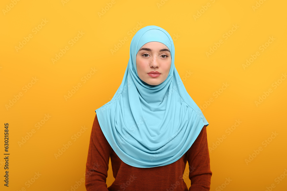 Wall mural Portrait of Muslim woman in hijab on orange background