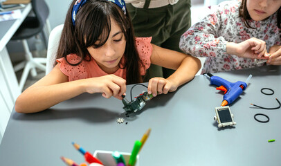 Portrait of concentrated female student screwing electrical circuit next to her teacher and to other schoolchild in a robotics class. Elementary technological education concept.