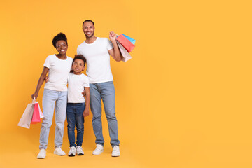 Family shopping. Happy parents and son with colorful bags on orange background, space for text - Powered by Adobe