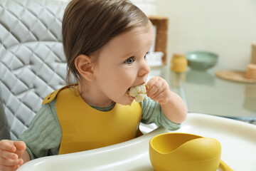 Cute little baby eating healthy food in high chair indoors