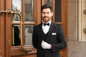 Butler in elegant suit and white gloves near wooden hotel door