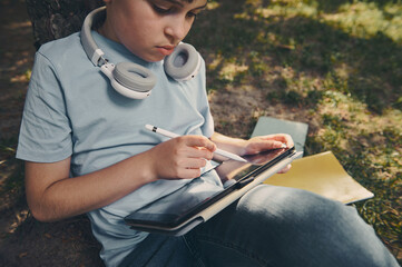 Handsome smart school boy using a digital tablet and stylus pen, drawing, sketching, enjoying his...