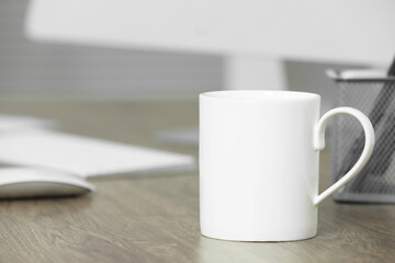 Fototapeta na wymiar White ceramic mug on wooden table at workplace. Mockup for design