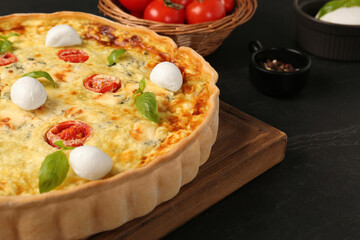 Delicious homemade cheese quiche and ingredients on black table, closeup