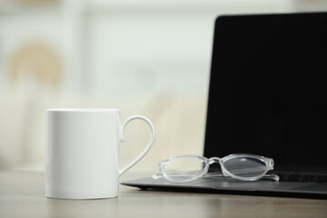 Obraz na płótnie Canvas White ceramic mug, glasses and laptop on wooden table indoors. Space for text