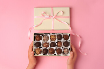 Child with box of delicious chocolate candies on pink background, top view