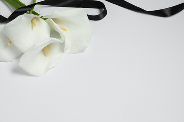 Beautiful calla lilies and black ribbon on white background, closeup with space for text. Funeral...