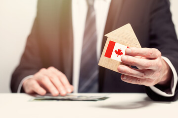 Businessman hand holding wooden home model with Canadian flag. insurance and property concepts