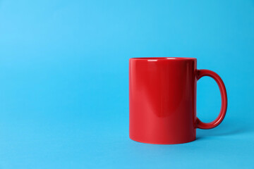 One red ceramic mug on light blue background. Space for text