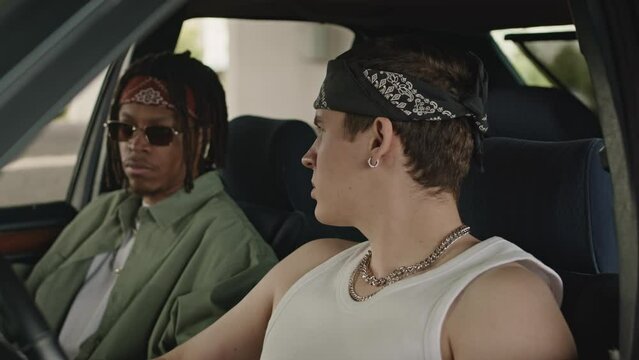 Ches up of Caucasian and African American dudes in bandanas on their heads talking while sitting in car parked outside