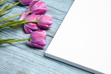Blank white canvas mockup with flowers on wood background. Single blank canvas on blue wall, corner closeup