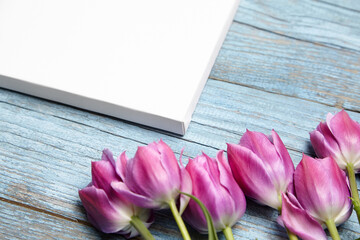 Blank white canvas mockup with flowers on blue wood background. Mockup with white canvas on wood