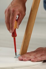 Man with screwdriver assembling furniture on floor indoors, closeup