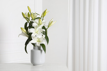 Beautiful bouquet of lily flowers in vase on light table near white wall, space for text
