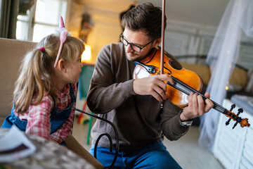 Music is so much fun. Young father teaching his little daughter to play violin and smiling. © NDABCREATIVITY
