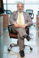 Senior indian businessman Sitting on chair and giving happy expression at office.