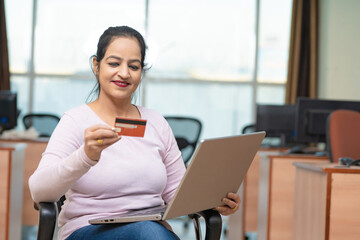 Indian woman using laptop and bank card at office
